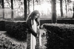 Lisette staat buiten op het kerkhof, ze kijkt naar beneden en houdt haar handen op haar zwangere buik.