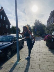 Lisette die tijdens het hardlopen een rek oefening doet bij een lantaarnpaal.